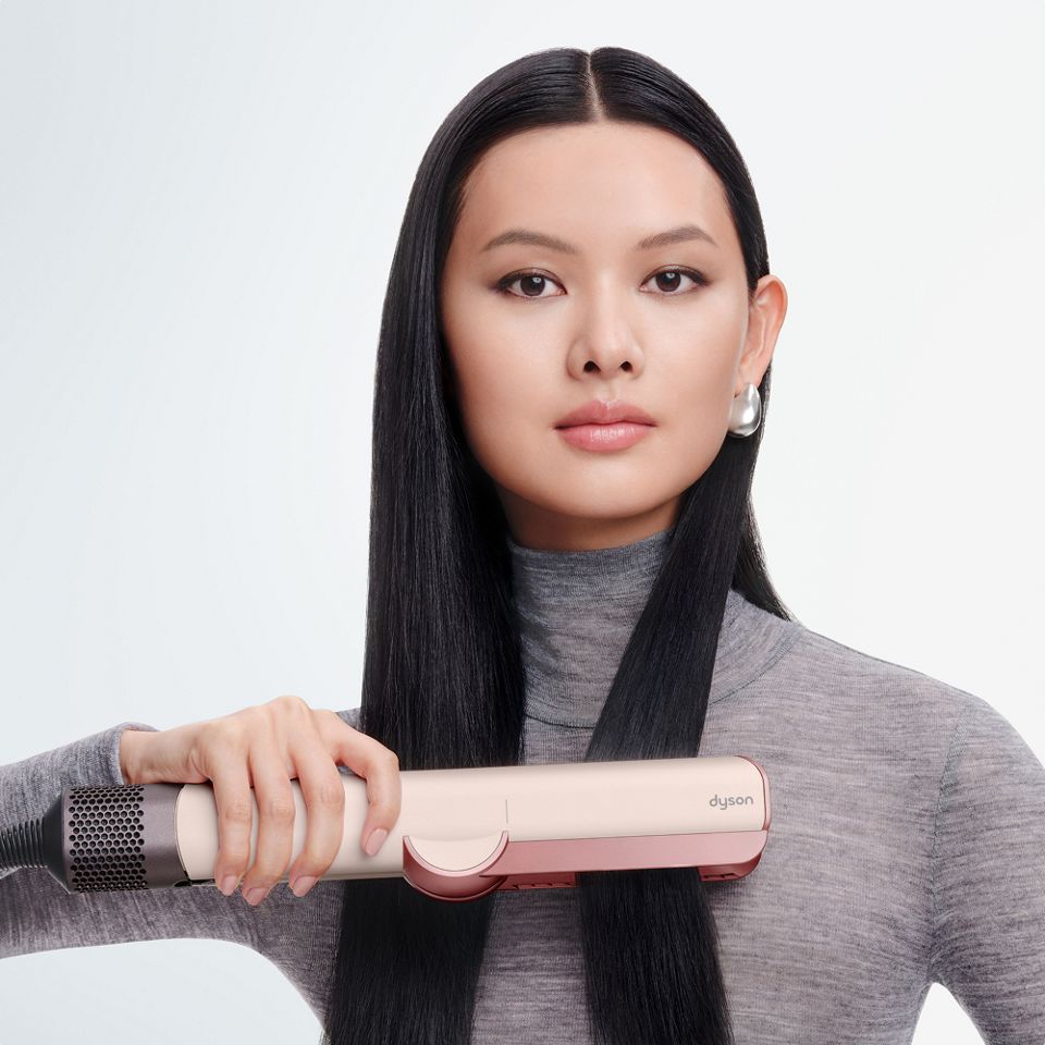 Модель разглаживает и выпрямляет волосы феном-выпрямителем Dyson Airstrait.