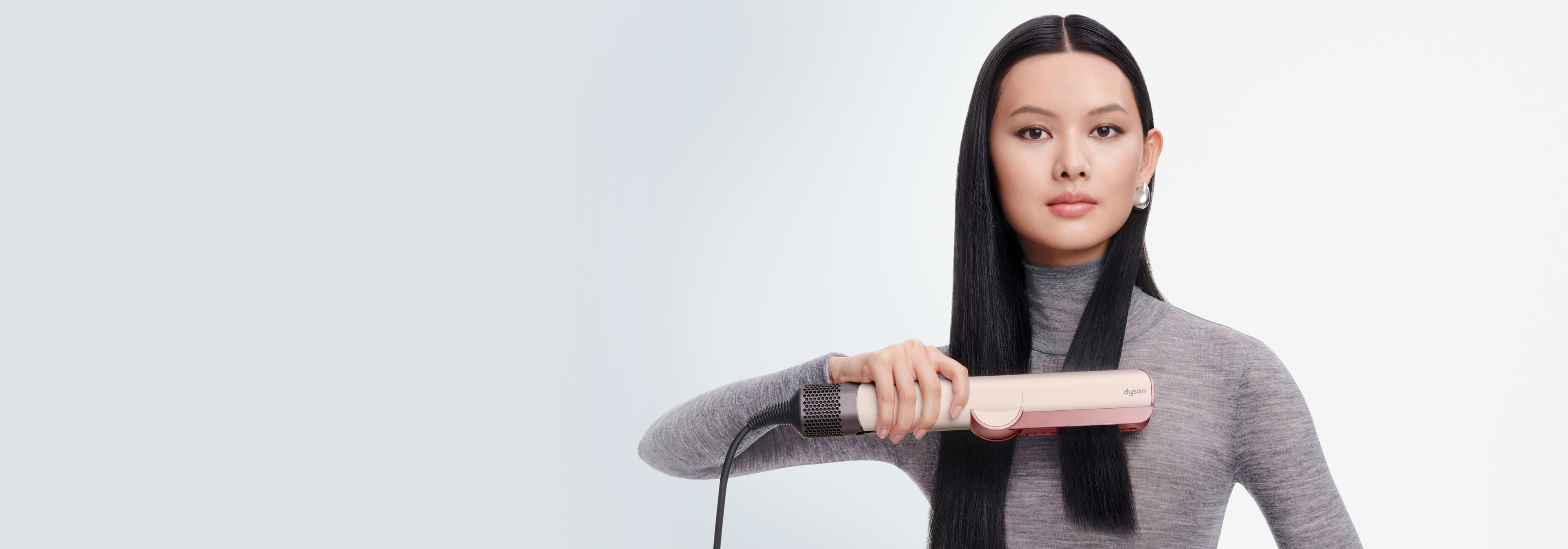 Модель выпрямляет волосы феном-выпрямителем Dyson Airstrait.
